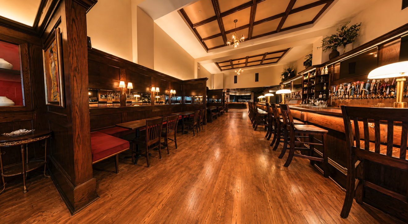 Wide view of the full venue interior — long bar, wood paneling and coffered ceiling