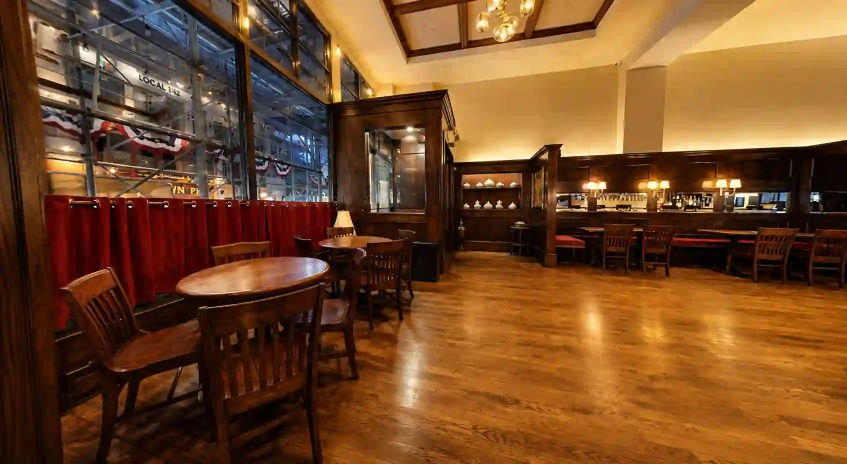Round tables by the tall street-facing windows with the service bar in the background