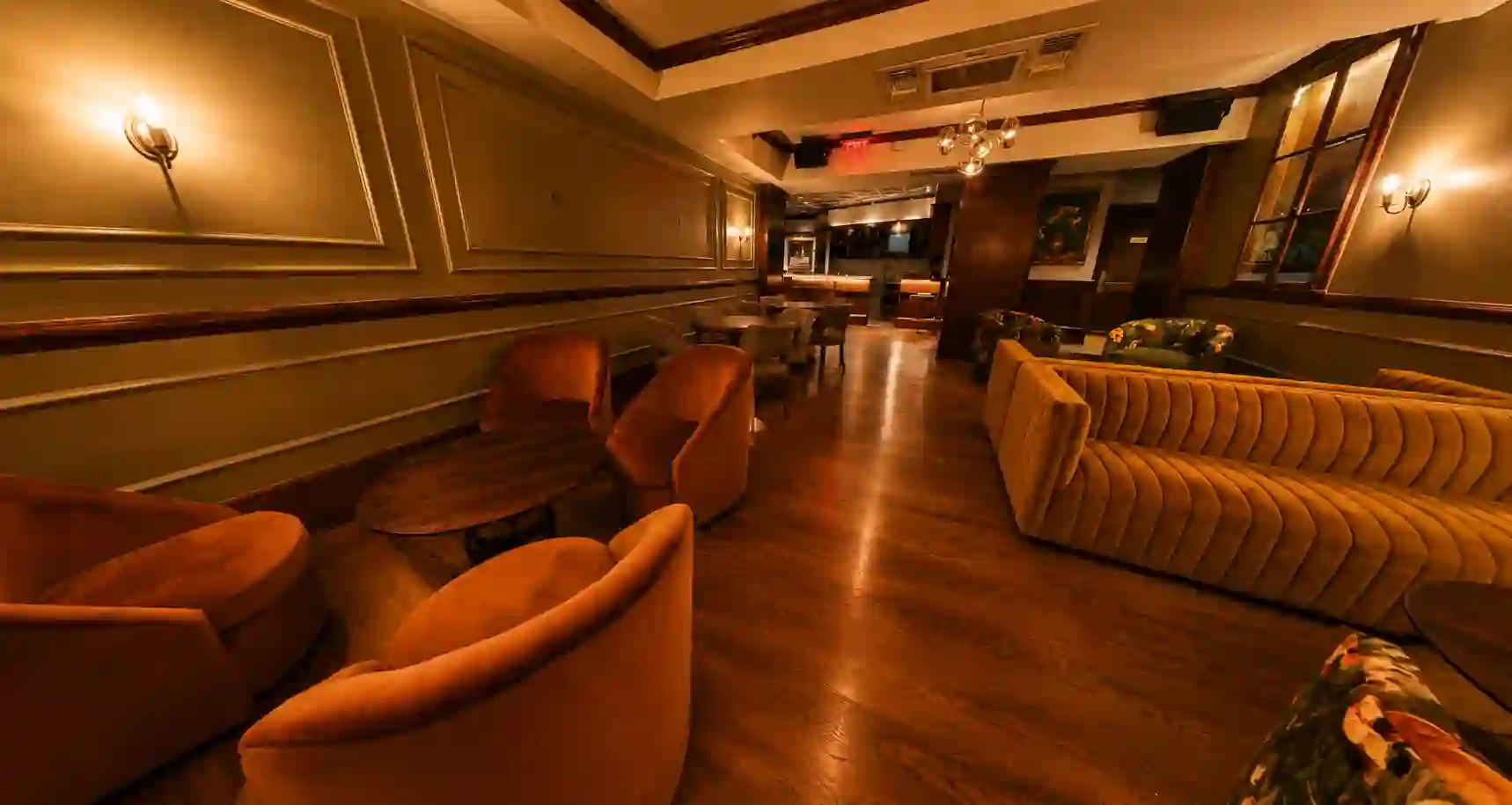 Private room lounge with velvet tub chairs, curved sofas and wall sconces